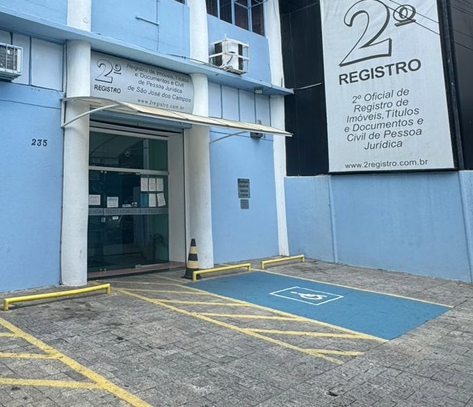 Fachada do cartório na R. Vilaça, 235: prédio azul-claro de dois andares com colunas brancas, entrada de vidro sob toldo, placa vertical “2º Registro” à direita e vaga de estacionamento acessível demarcada em azul no pátio em frente.